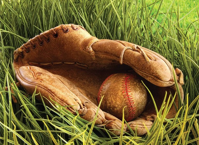A baseball glove and ball in the grass.